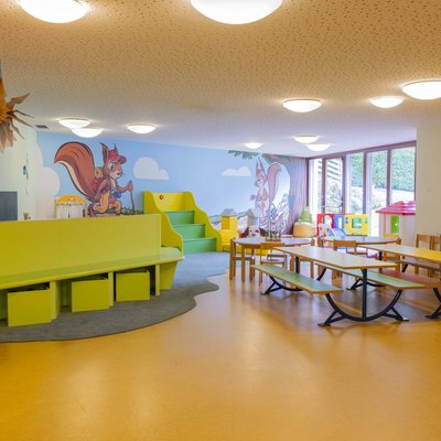 Alpine Stays for all Generations by Family Rainer Buntes Kinderspielzimmer mit Tischen, Stühlen und Wandmalerei von Eichhörnchen