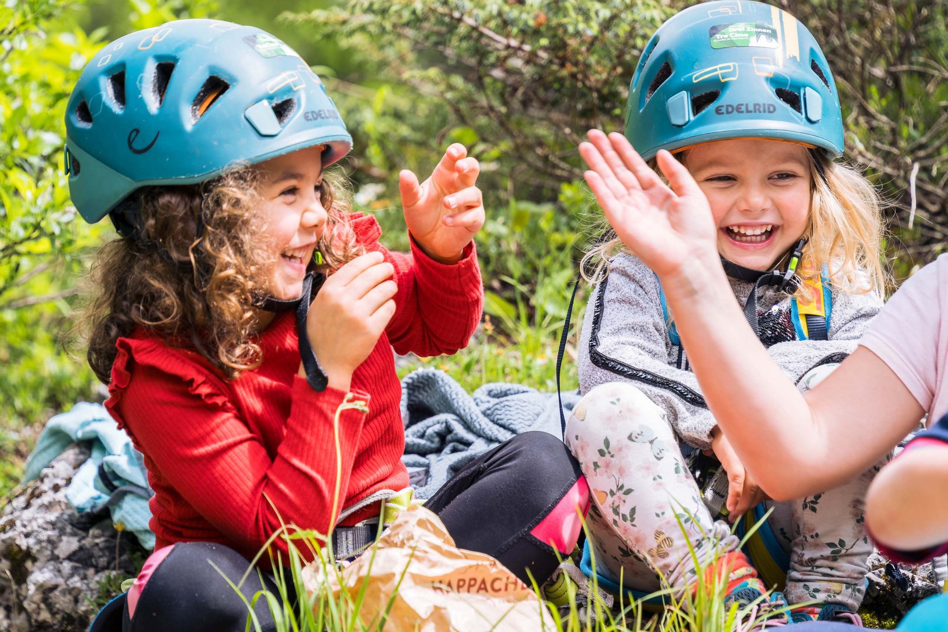 Your family resort in the Dolomites Children wearing climbing helmets laughing and sitting on grass outdoors