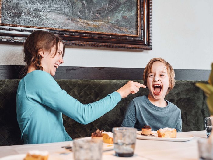 Your family resort in the Dolomites Woman playfully touching laughing boy's face at restaurant table