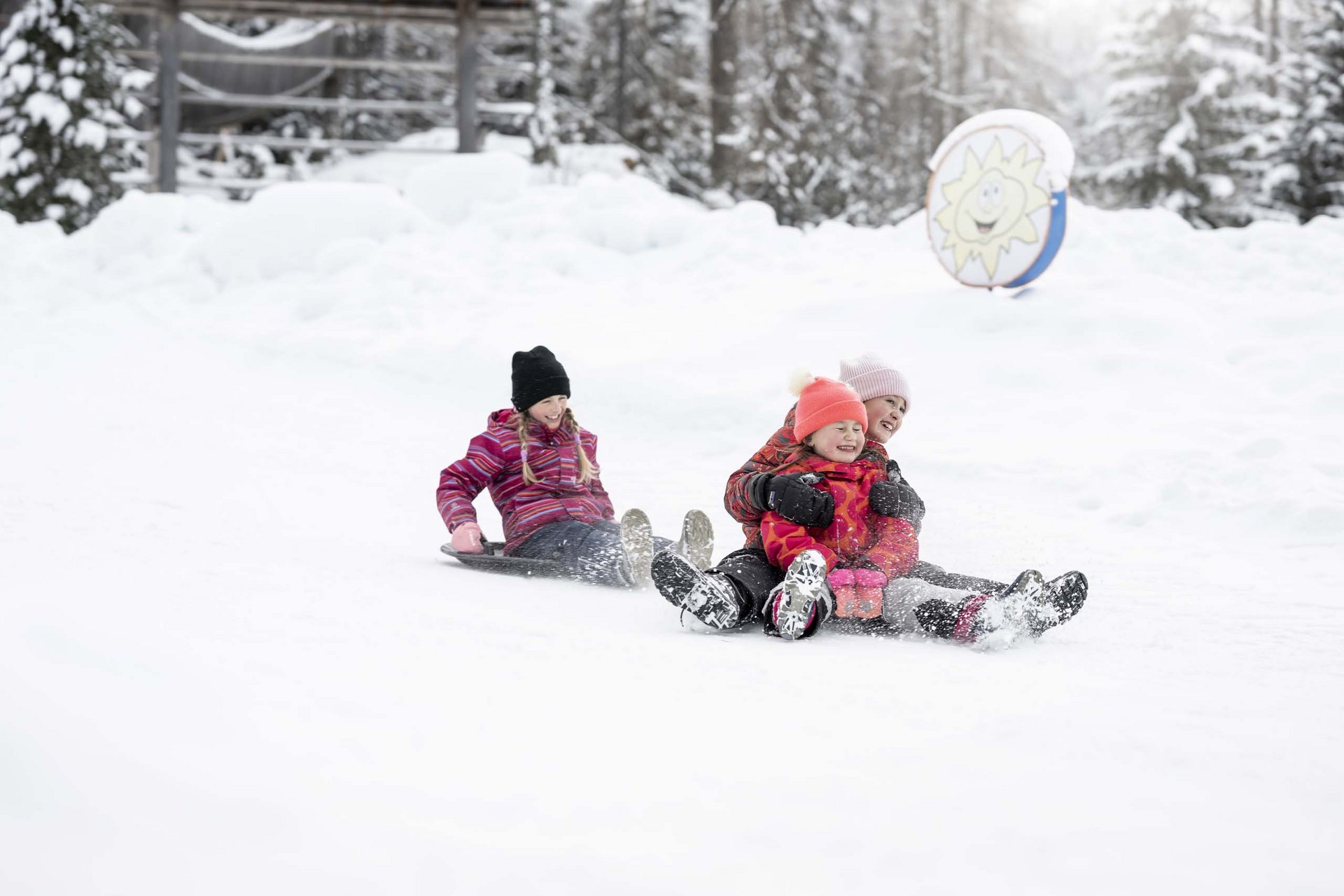 Experience exciting adventures with Raini! Three children sledding together in the snowy winter forest.