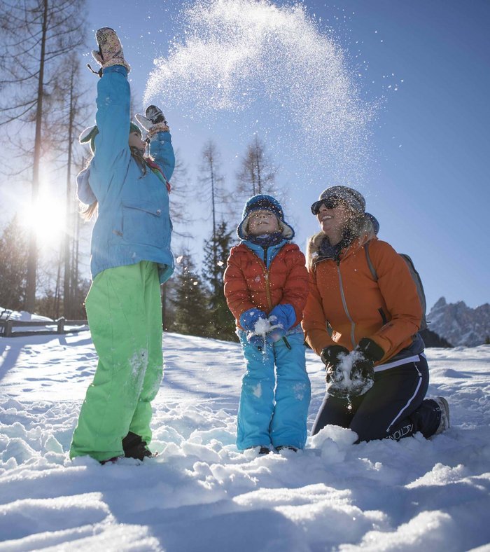 Alpine Stays for all Generations by Family Rainer Familie spielt im Schnee bei sonnigem Wintertag im Wald