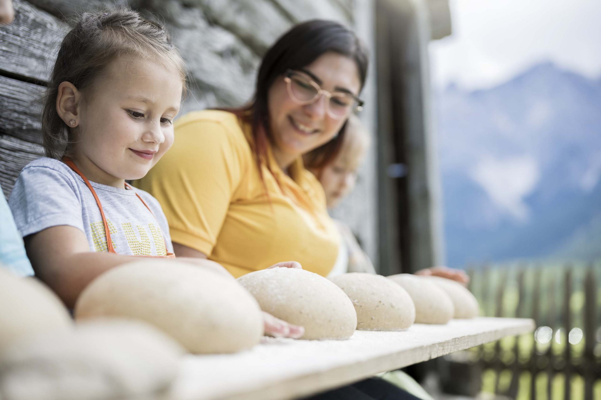 Your family resort in the Dolomites Child and adult shaping bread dough balls on a wooden board outdoors