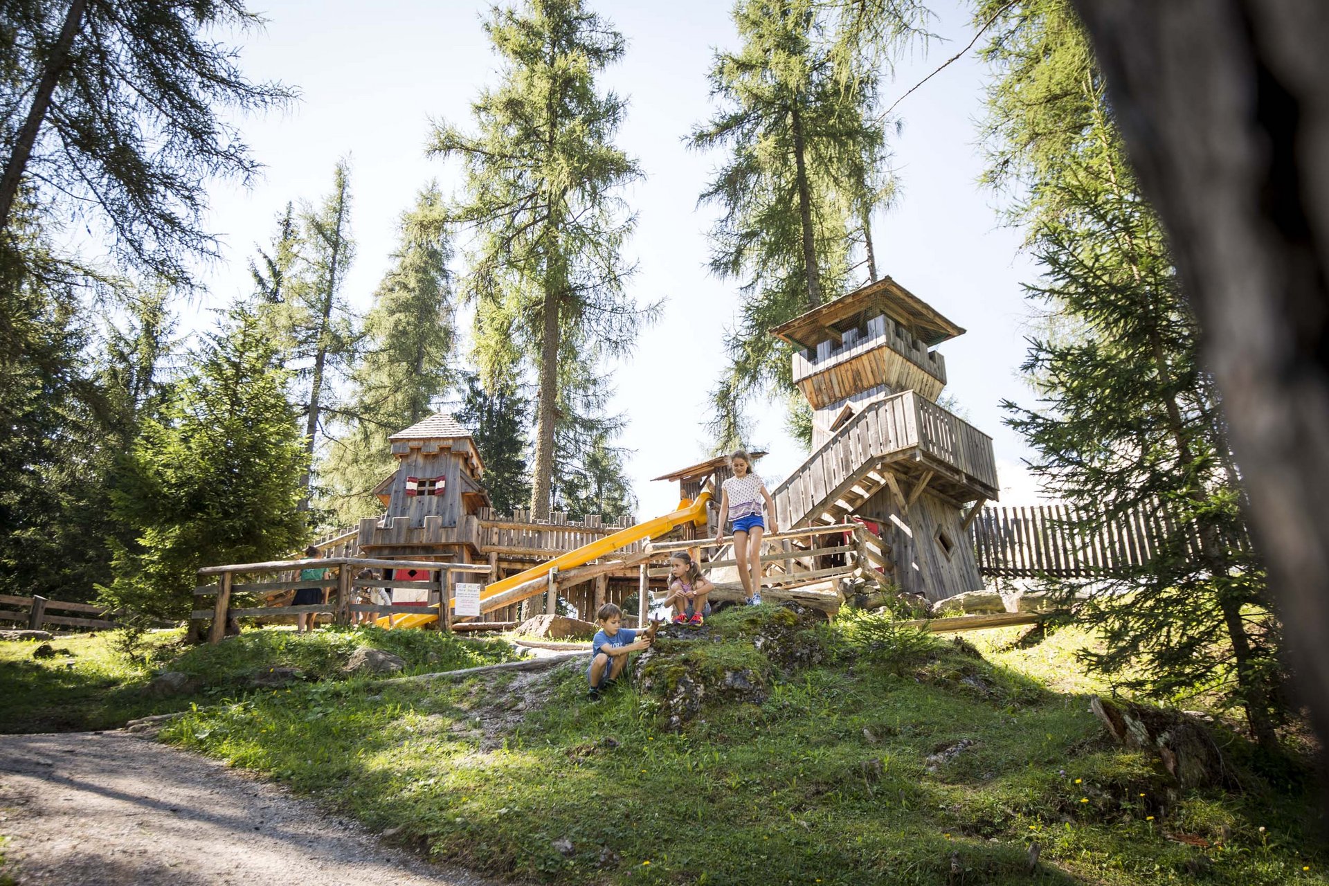 Experience exciting adventures with Raini! Children playing on a wooden playground with a slide in the forest