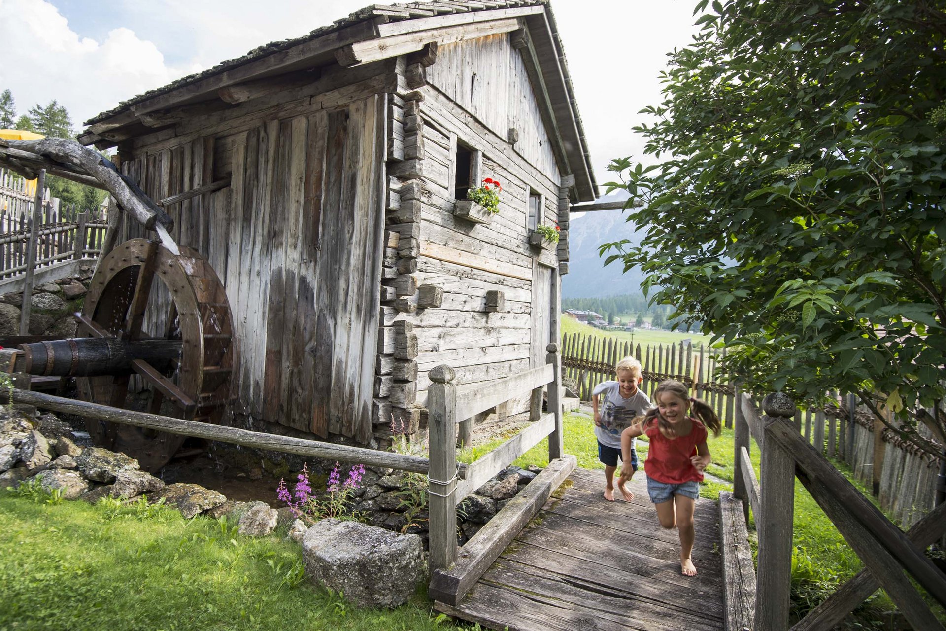 Experience exciting adventures with Raini! Barefoot children running next to an old watermill house in a rural setting