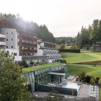 1 Familienhotel in Südtirol und 3 Residences: Family Resort Rainer Hotelgebäude mit Balkon und großem Rasen vor Berglandschaft unter blauem Himmel