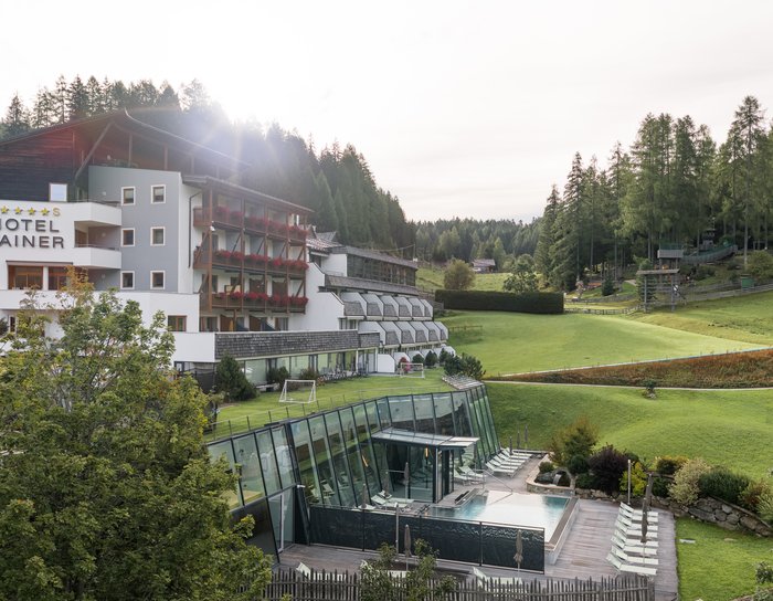 1 Familienhotel in Südtirol und 3 Residences: Family Resort Rainer Hotelgebäude mit Balkon und großem Rasen vor Berglandschaft unter blauem Himmel