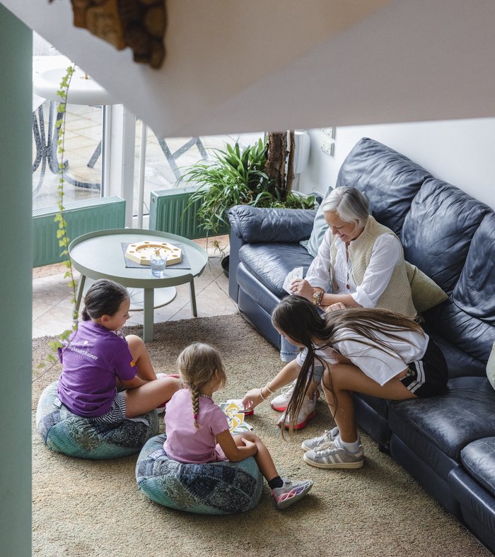 1 Familienhotel in Südtirol und 3 Residences: Family Resort Rainer Drei Frauen und ein Mädchen spielen mit Karten im Wohnzimmer, während eine ältere Frau zusieht