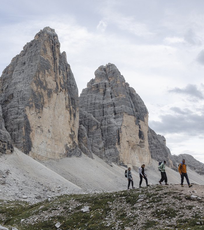 1 Familienhotel in Südtirol und 3 Residences: Family Resort Rainer Zwei Wanderer sitzen auf Felsen mit Blick auf die Dolomiten und bewölkten Himmel