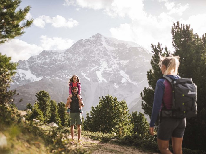 Your active family holiday in the Dolomites Man carrying child on shoulders hiking with woman in front of snowy mountains