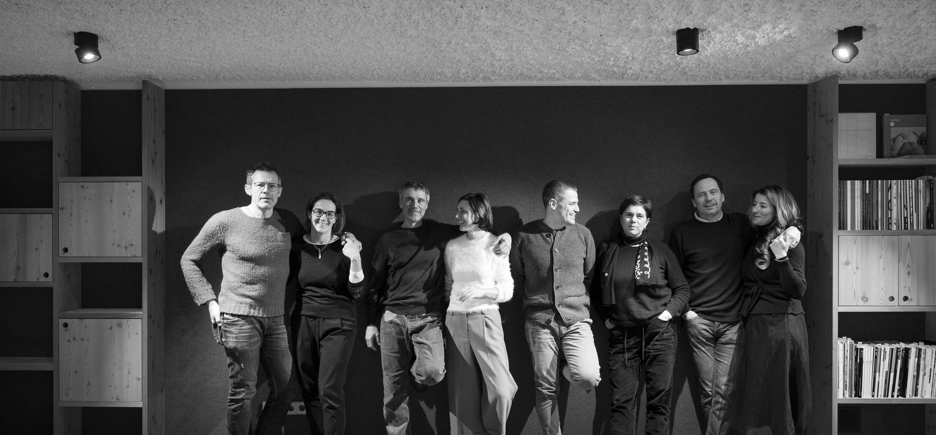 Your family resort in the Dolomites Eight people standing casually against a wall, smiling and relaxed