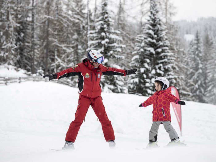 Your active family holiday in the Dolomites Ski instructor teaching child in red jacket to ski in the snow