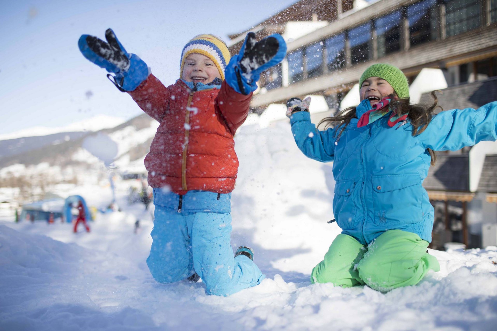 Your family resort in the Dolomites Two children happily playing in the snow in front of a building