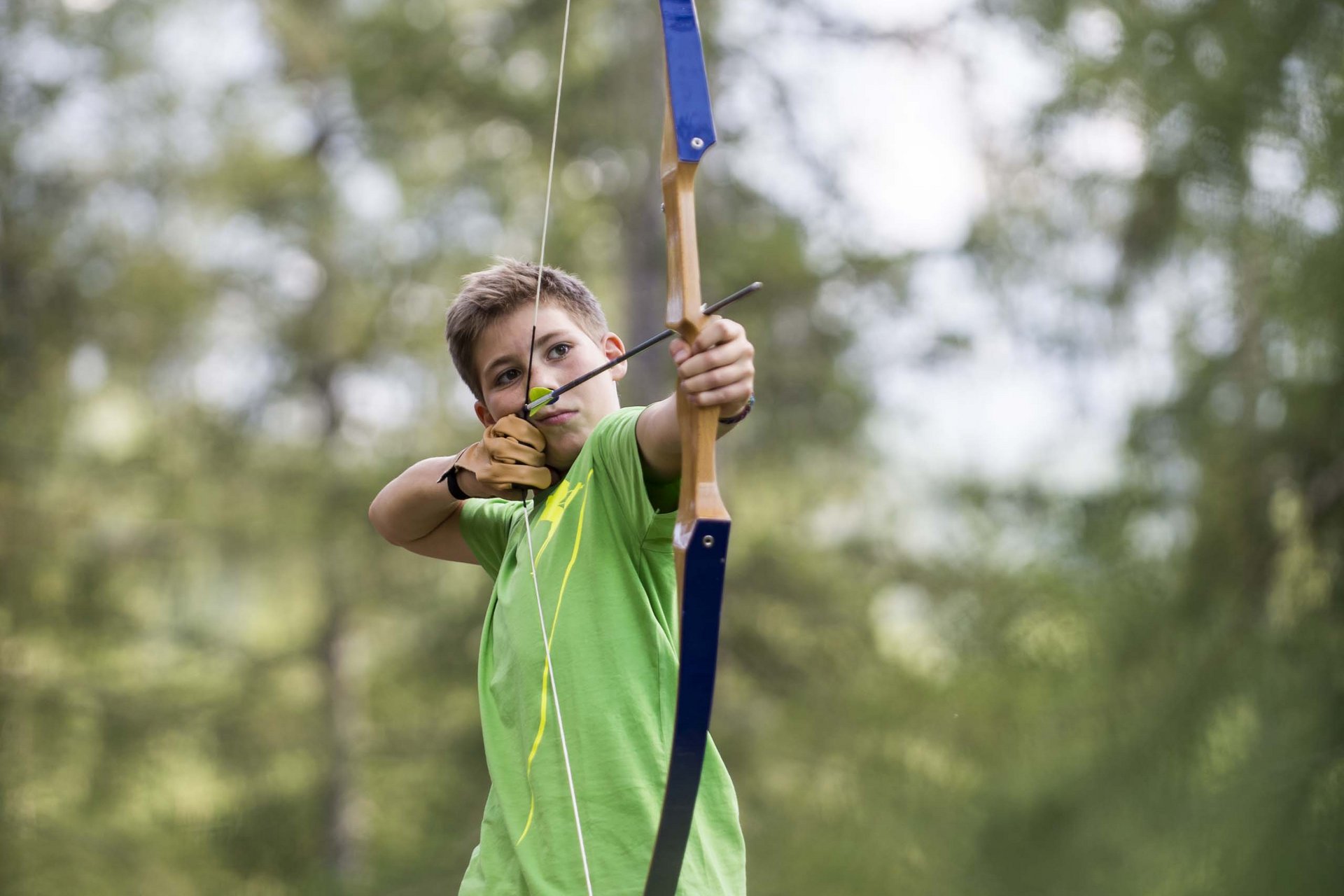 Experience exciting adventures with Raini! Boy aiming with bow and arrow in the forest