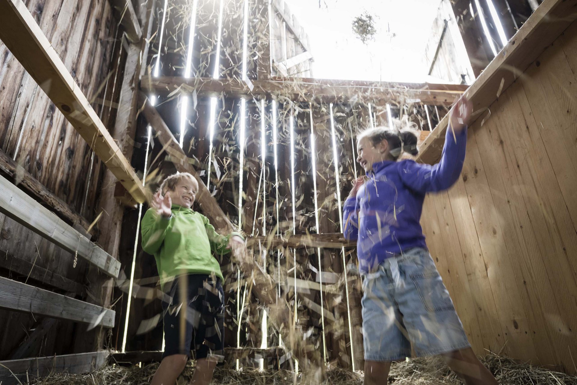 Your family resort in the Dolomites Two children laughing and playing with hay in a barn