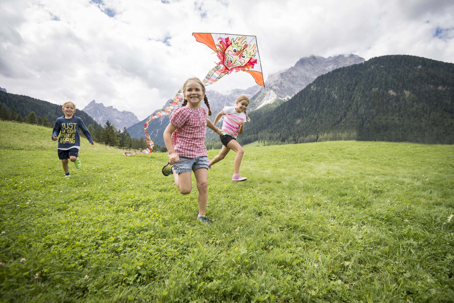 Your family resort in the Dolomites Children running on a meadow flying a dragon-headed kite