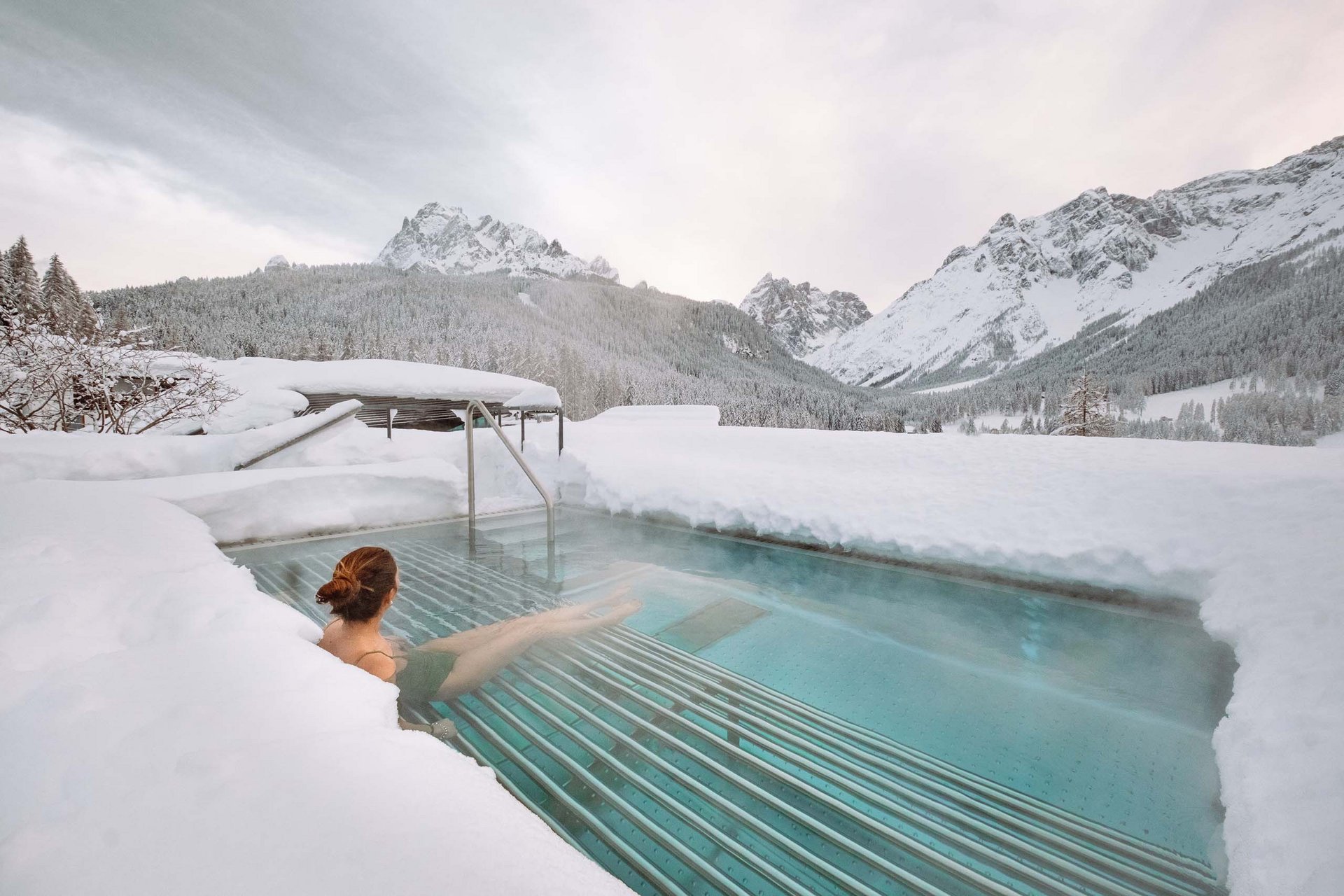 Stylish holidays at the Residence Paramount Alma Woman relaxing in heated outdoor pool surrounded by snowy mountains