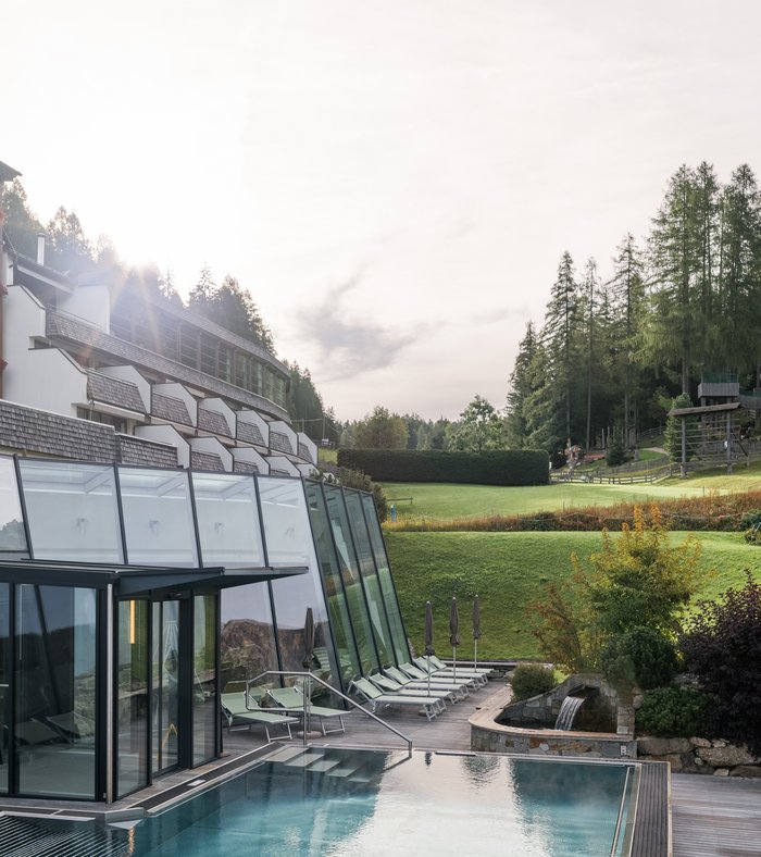 1 Familienhotel in Südtirol und 3 Residences: Family Resort Rainer Außenpool mit Liegestühlen und Sonnenschirmen bei sonnigem Himmel und grüner Landschaft