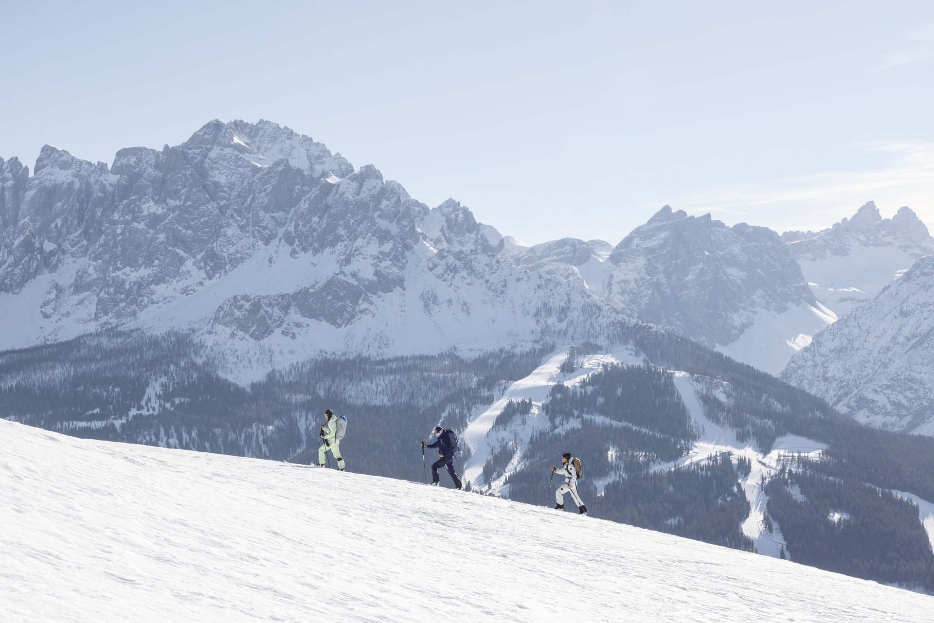 1 Familienhotel in Südtirol und 3 Residences: Family Resort Rainer Drei Personen steigen mit Stöcken einen verschneiten Hang vor einer Bergkulisse hinauf