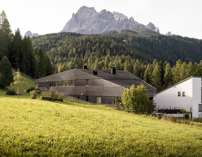 1 Familienhotel in Südtirol und 3 Residences: Family Resort Rainer Moderne Gebäude mit Garten und Bergen im Hintergrund an einem sonnigen Tag