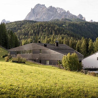 1 Familienhotel in Südtirol und 3 Residences: Family Resort Rainer Moderne Gebäude mit Garten und Bergen im Hintergrund an einem sonnigen Tag