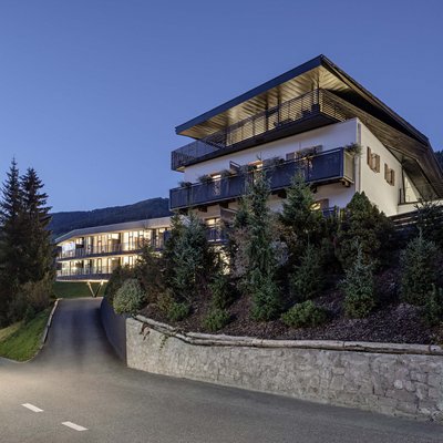 Alpine Stays for all Generations by Family Rainer Modernes Hotelgebäude bei Dämmerung in bergiger Landschaft