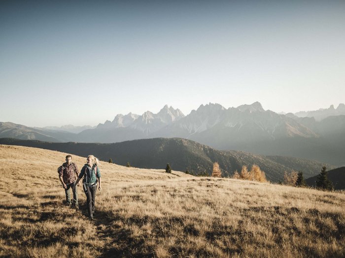 True adventure at our family hotel in the Dolomites! Two hikers on a grassy field with mountain range in background