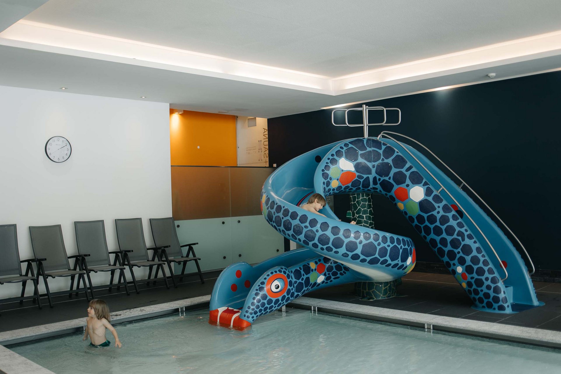 Your family resort in the Dolomites Children playing on a water slide in an indoor pool