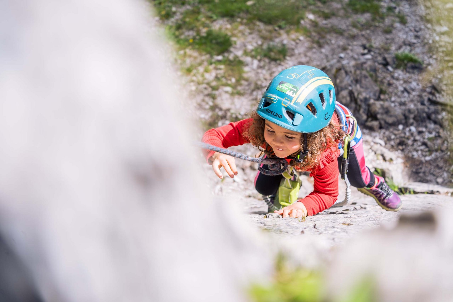 Your active family holiday in the Dolomites Child with helmet climbing a secured rock wall outdoors