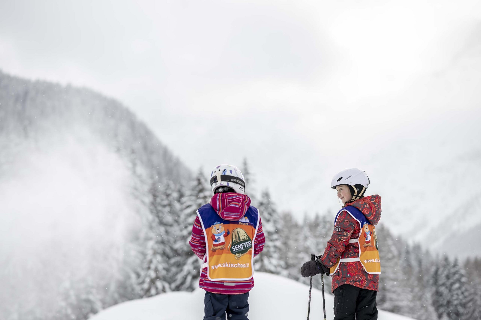 Your family resort in the Dolomites Two children in ski gear and orange vests on a snowy slope