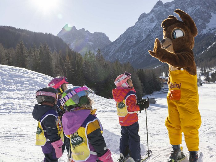 Experience exciting adventures with Raini! Kids in ski gear learning with a bear mascot on the snow