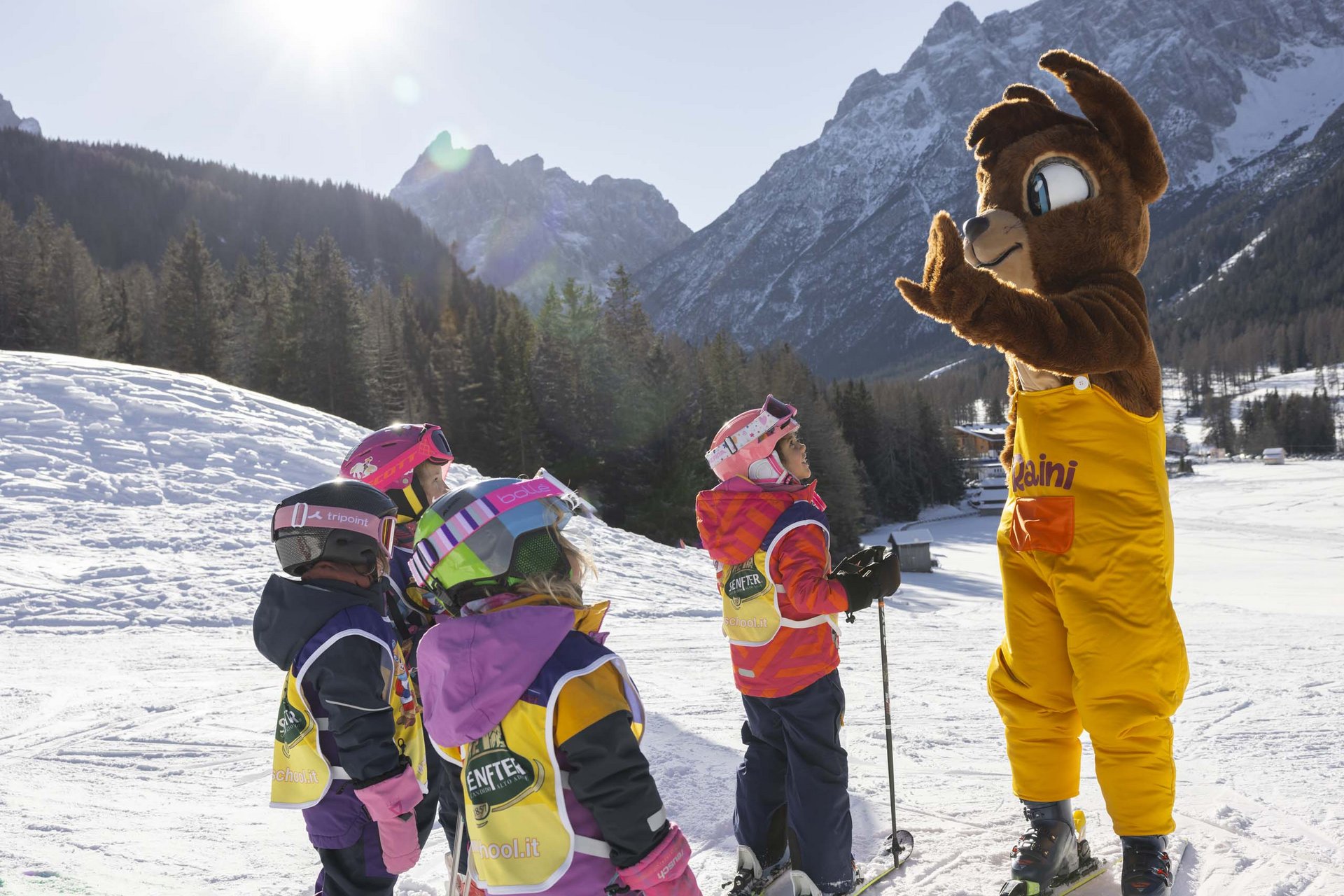 Your family resort in the Dolomites Kids in ski gear learning with a bear mascot on the snow