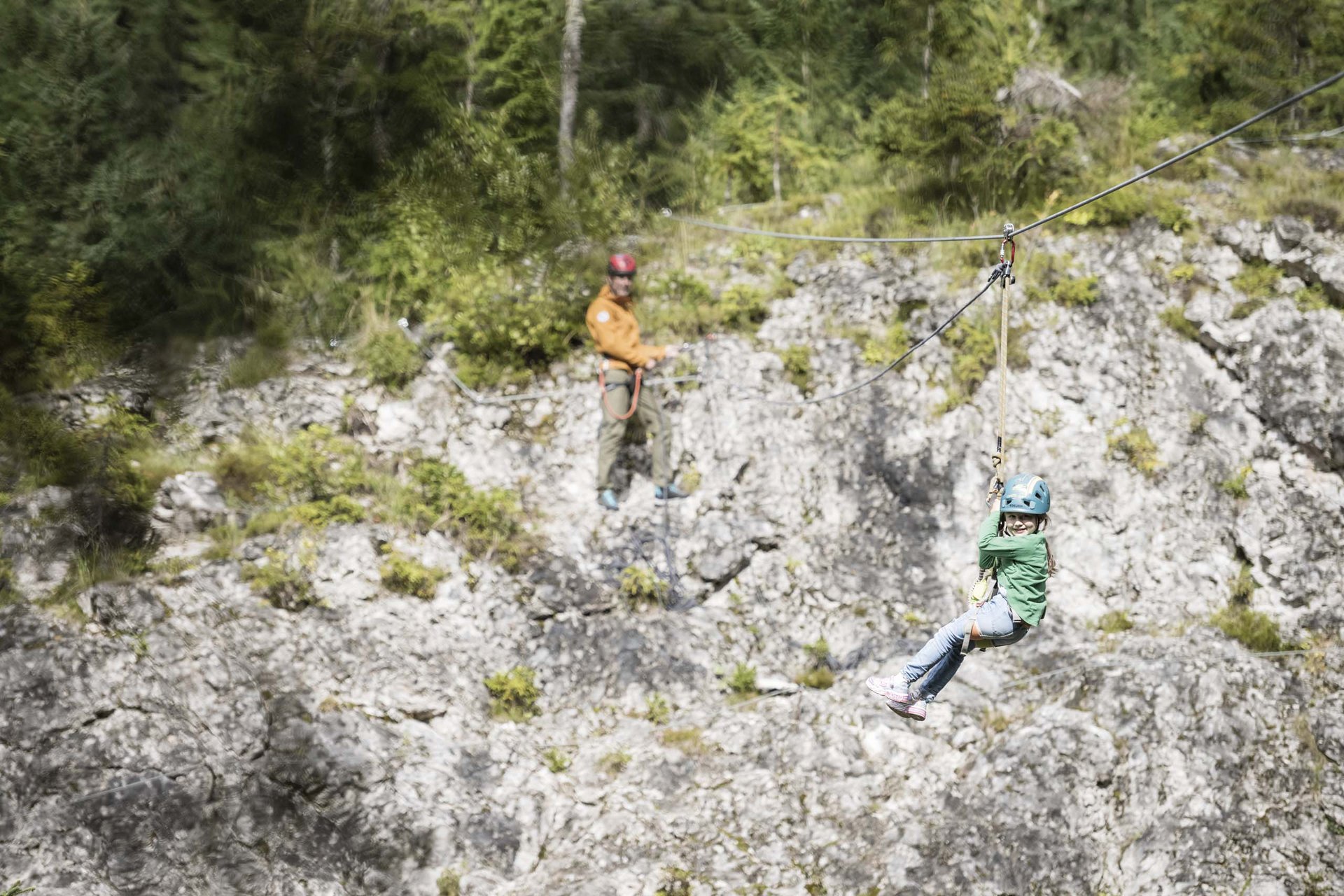 Your family resort in the Dolomites Child with helmet on zipline above rocky forest slope