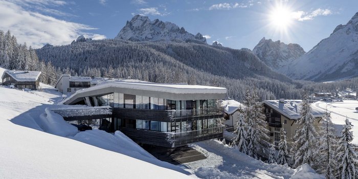 Alpine Stays for all Generations by Family Rainer Modernes Hotel im Schnee vor verschneiten Bergen und klarem Himmel