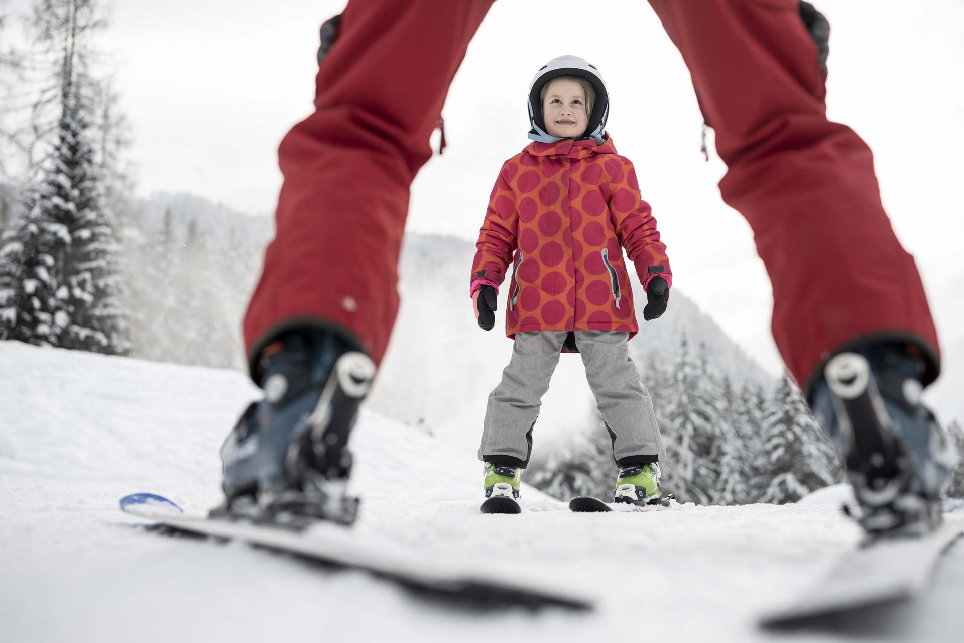 Experience exciting adventures with Raini! Child learning to ski with instructor on snowy mountain