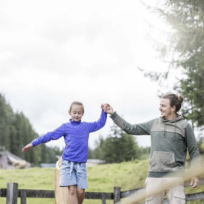 Alpine Stays for all Generations by Family Rainer Vater hilft Tochter beim Balancieren auf Slackline im Freien