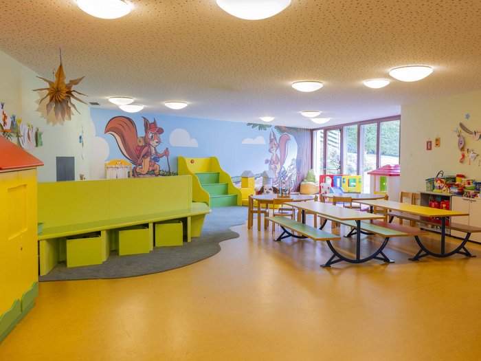 Experience exciting adventures with Raini! Colorful kindergarten room with tables, benches, and children's drawings on walls