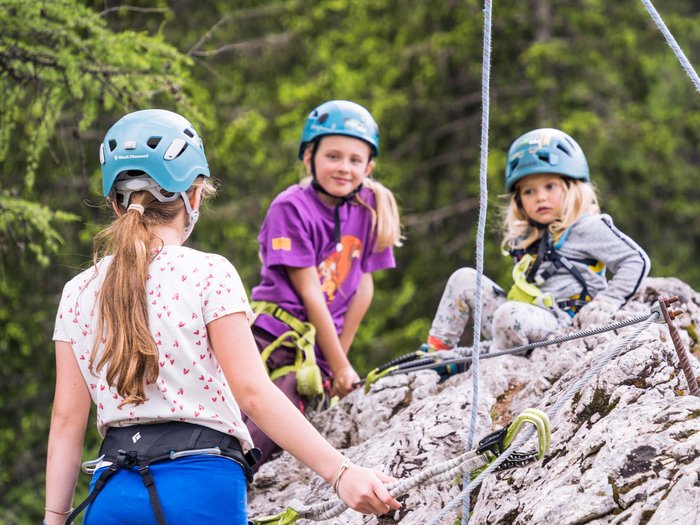 L’hotel con assistenza ai bambini in Alto Adige Tre bambini con caschi arrampicati su rocce in foresta